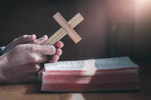 praying hands holding a cross over an open Bible 