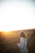 a woman looking out into a field at sunset 