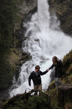 couple hiking up a mountain near a waterfall 