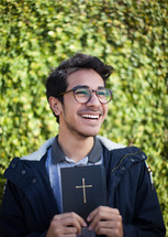 a smiling man holding a Bible outdoors 