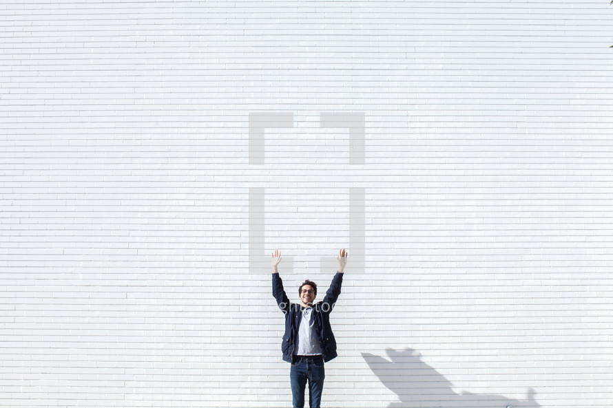 man standing in front of a white wall with hands raised 
