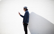 a man looking at his cellphone standing in front of a white wall 