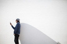 man standing in front of a white wall looking at his cellphone screen 