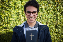 a smiling man holding a Bible outdoors 