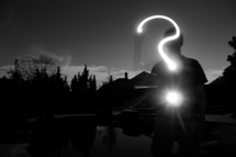 Silhouette of a teen making a question mark with a light.