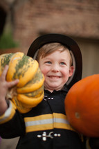 a boy child in a costume holding a pumpkin