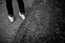 A teen girl's feet standing on asphalt.