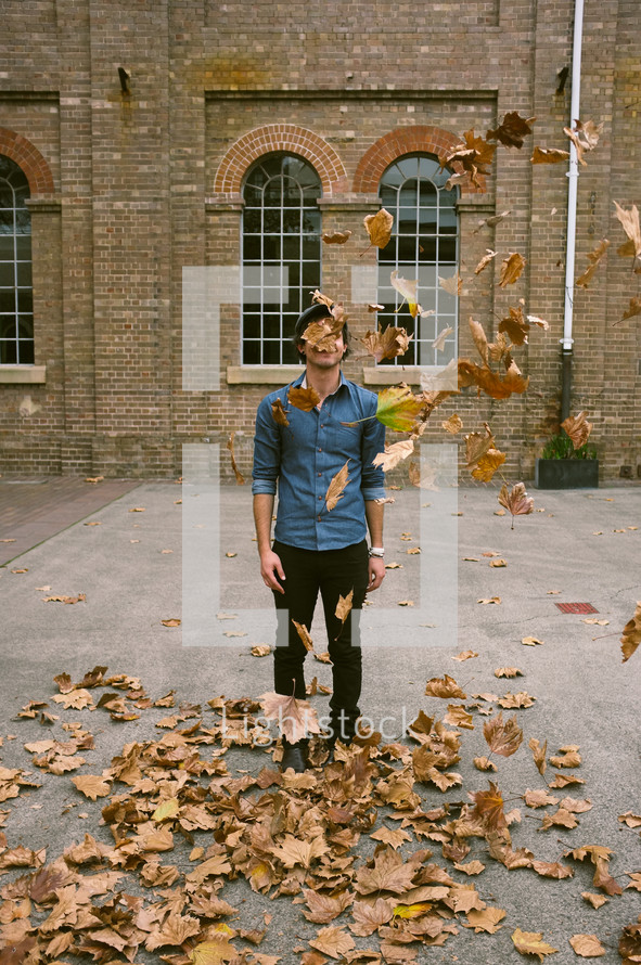 man tossing fall leaves into the air 