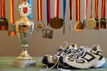 A pair of running shoes next to a trophy and medals.