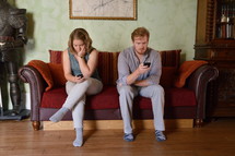 A couple sitting on a sofa looking at their cell phones and ignoring each other.