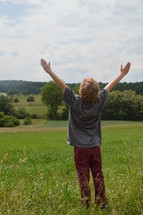 child with raised arms in adoration outdoors at a meadow. 