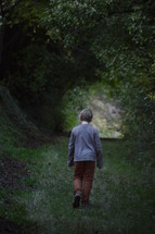 little boy walking alone through a dark ravine forest in late evening
