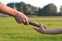 woman giving the relay baton to the next generation into a child's hand