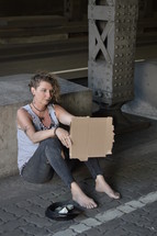 homeless woman holding a blank sign begging under a bridge 