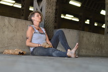 a woman sitting under a bridge with bottle of alcohol 
