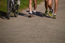 joggers on a running trail with a bicycle besides