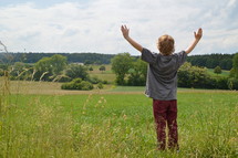 child with raised arms in adoration outdoors at a meadow. 
