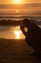man praying at the beach in front of a sunset

