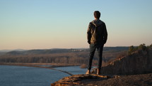 a man standing at the edge of a cliff looking out at a river below 