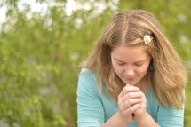 Young blond woman praying outdoors. 