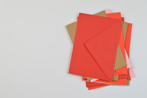 stacked envelope - pile of red, pink and brown envelopes on white background with copy space to the left  
