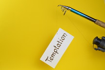 A fishing pole with a piece of paper with the word temptation on it 