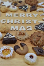 different kinds of Christmas cookies on a breadboard around the words: MERRY CHRISTMAS