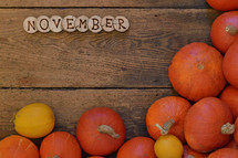 Pumpkins on wooden planks with pieces of wood spelling the word NOVEMBER. 