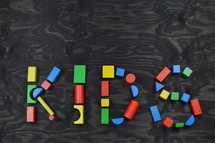 the word KIDS out of colorful wooden toy blocks on black wooden background
