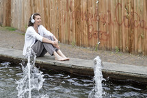 woman with headphones sitting by a reflection pool 