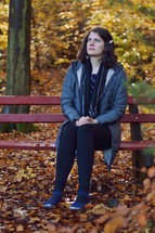 a woman praying on a bench in a park in fall 