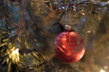 The Nativity story written in golden letters on a red Christmas ornament bulb hanging in a Christmas tree. 