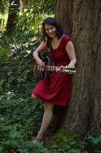 woman standing under a tree with a guitar 