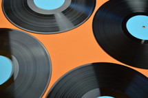 four old black vinyl records with blank cyan labels on orange background