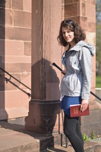 a woman standing on church steps holding a Bible 