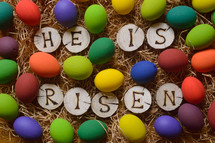 the words: HE HAS RISEN burned in wooden slieces between colorful painted eggs in straw 