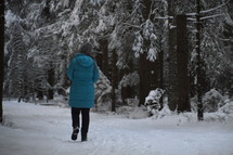 a woman in a coat walking through the snow in a winter forest 
