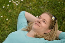 Young woman laying relaxed and daydreaming with open eyes in a meadow. 
