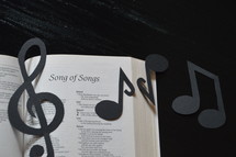 The Bible open to Song of Songs with paper musical notes covering it.