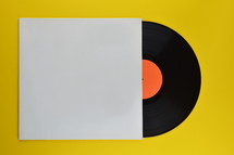 old black vinyl record with blank orange label halfway out of its white blank cover on yellow background 