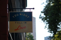 A sign hanging from a building that says, "You might fall in love."