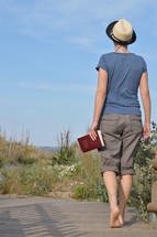 woman walking with bible in hand in the dunes near the beach