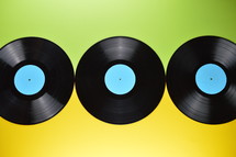 three old black vinyl records with blank cyan labels on yellow and green background
