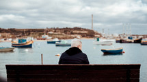 a man sitting on a bench looking out at the boats 