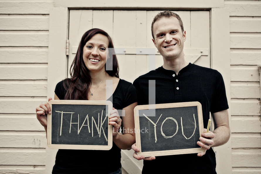 man and woman, standing in front of wood building holding thank you sign