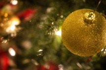 Gold glitter ball ornament hanging on Christmas tree.