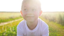 Closeup face of little boy looking to camera on the nature. Child boy smile in sunlight outdoors. Cute boy looking at camera while standing on sunset.