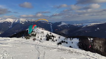 Winter paragliding proximity fly over snowy hill
