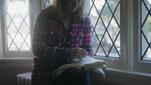 a woman praying at a window and reading a Bible 