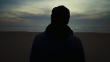 a man walking on a beach in a jacket with his back to the camera